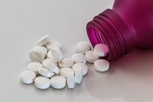 Some round white tablets spilling out of a pink pill bottle